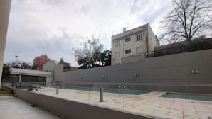 Un espace extérieur avec une piscine, une terrasse carrelée, un petit muret et une vue sur les bâtiments environnants.