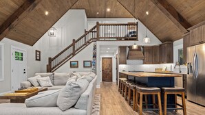 A spacious loft with a high ceiling, a wooden staircase, a kitchen with a central island, and a cozy seating area with a sofa and cushions. - Gorgeous Lakehouse, Sandy Bottom, Dock, AC (Lac du Flambeau)