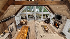 A spacious loft with a high ceiling, large windows, a stone fireplace, and a cozy seating area. - Gorgeous Lakehouse, Sandy Bottom, Dock, AC (Lac du Flambeau)