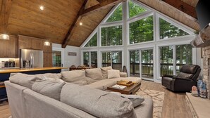 A spacious living area with a large sectional sofa, a leather armchair, and a coffee table. A wooden dining table with chairs is visible in the background. - Gorgeous Lakehouse, Sandy Bottom, Dock, AC (Lac du Flambeau)