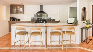 Cozinha moderna com ilha central, banquetas, exaustor preto e janela com vista para a cidade.