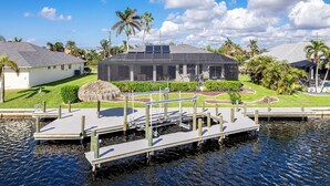 A waterfront property with a dock, a house with a solar panel roof, and surrounding greenery. - Your Waterfront Oasis | Private Pool, Dock, Canal | Gulf Access (Cape Coral)