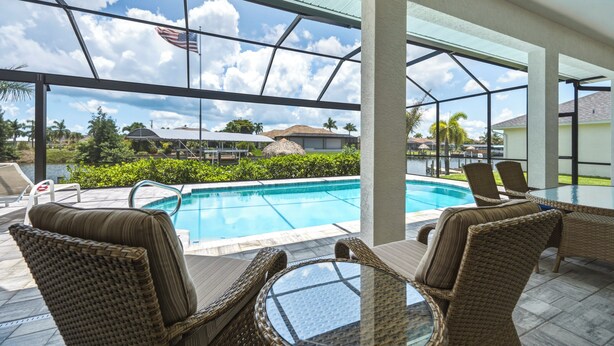 A covered outdoor area with a pool, wicker furniture, and a view of the surrounding landscape. - Your Waterfront Oasis | Private Pool, Dock, Canal | Gulf Access (Cape Coral)