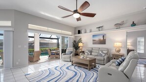A spacious living room with a large window, a ceiling fan, and a view of a pool. - Your Waterfront Oasis | Private Pool, Dock, Canal | Gulf Access (Cape Coral)
