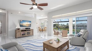 A spacious living room with a ceiling fan, a television, a wooden coffee table, and a view of the outdoors through large sliding doors. - Your Waterfront Oasis | Private Pool, Dock, Canal | Gulf Access (Cape Coral)
