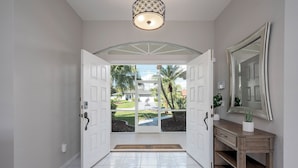 A hallway with a white door leading to a patio with a view of a house and palm trees. - Your Waterfront Oasis | Private Pool, Dock, Canal | Gulf Access (Cape Coral)