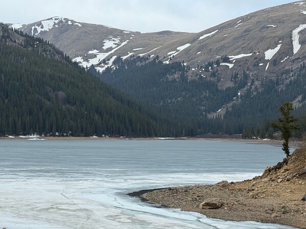 A lake surrounded by mountains with snow patches and dense forests.
