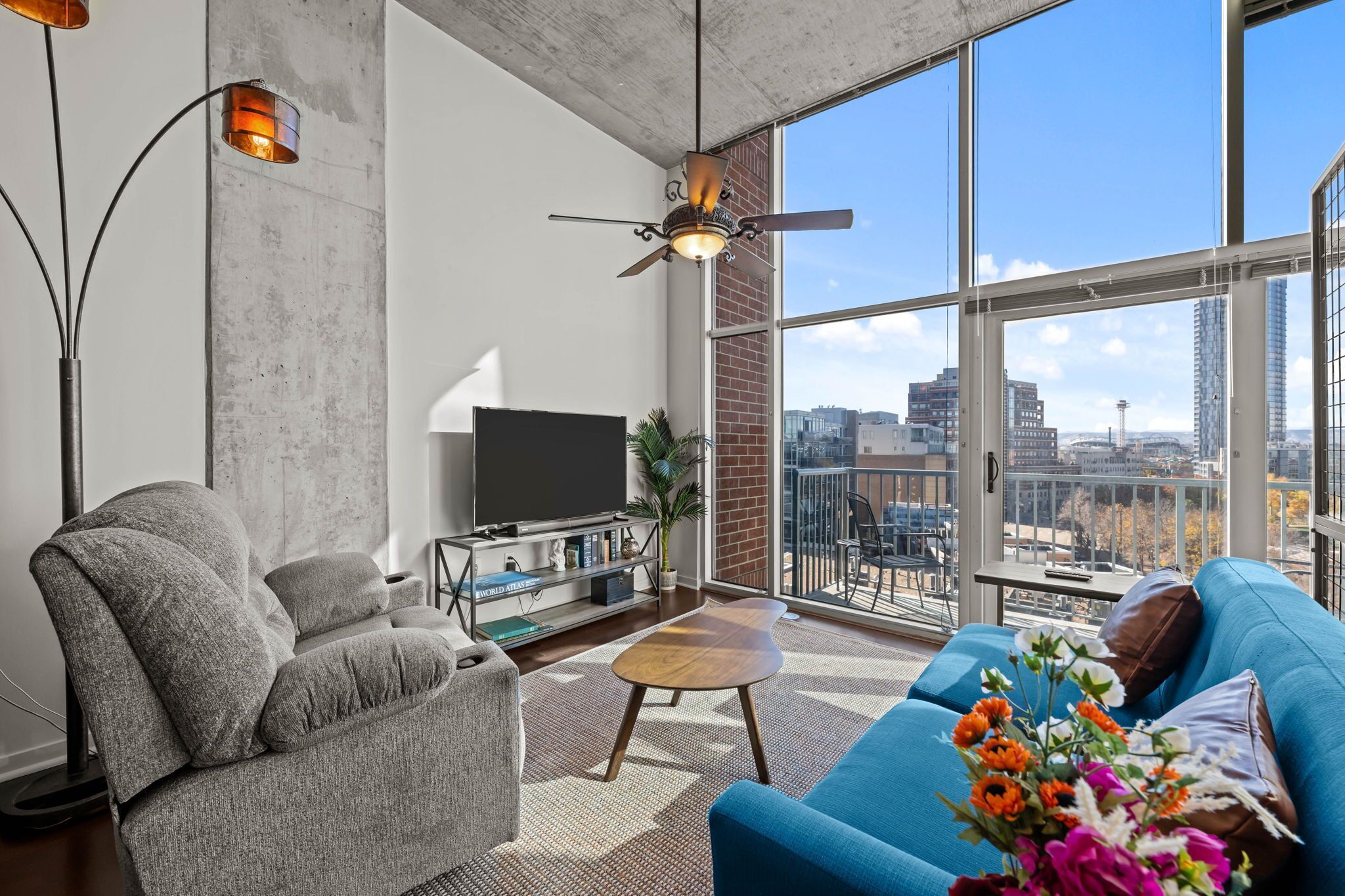A modern living room with a sofa, armchair, and coffee table, a flat-screen TV, and a large window with a city view.