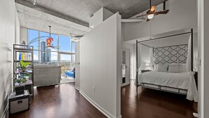 Ein modernes Schlafzimmer mit großem Fenster, einem Bett mit gemustertem Kopfteil und Blick auf die Stadt.