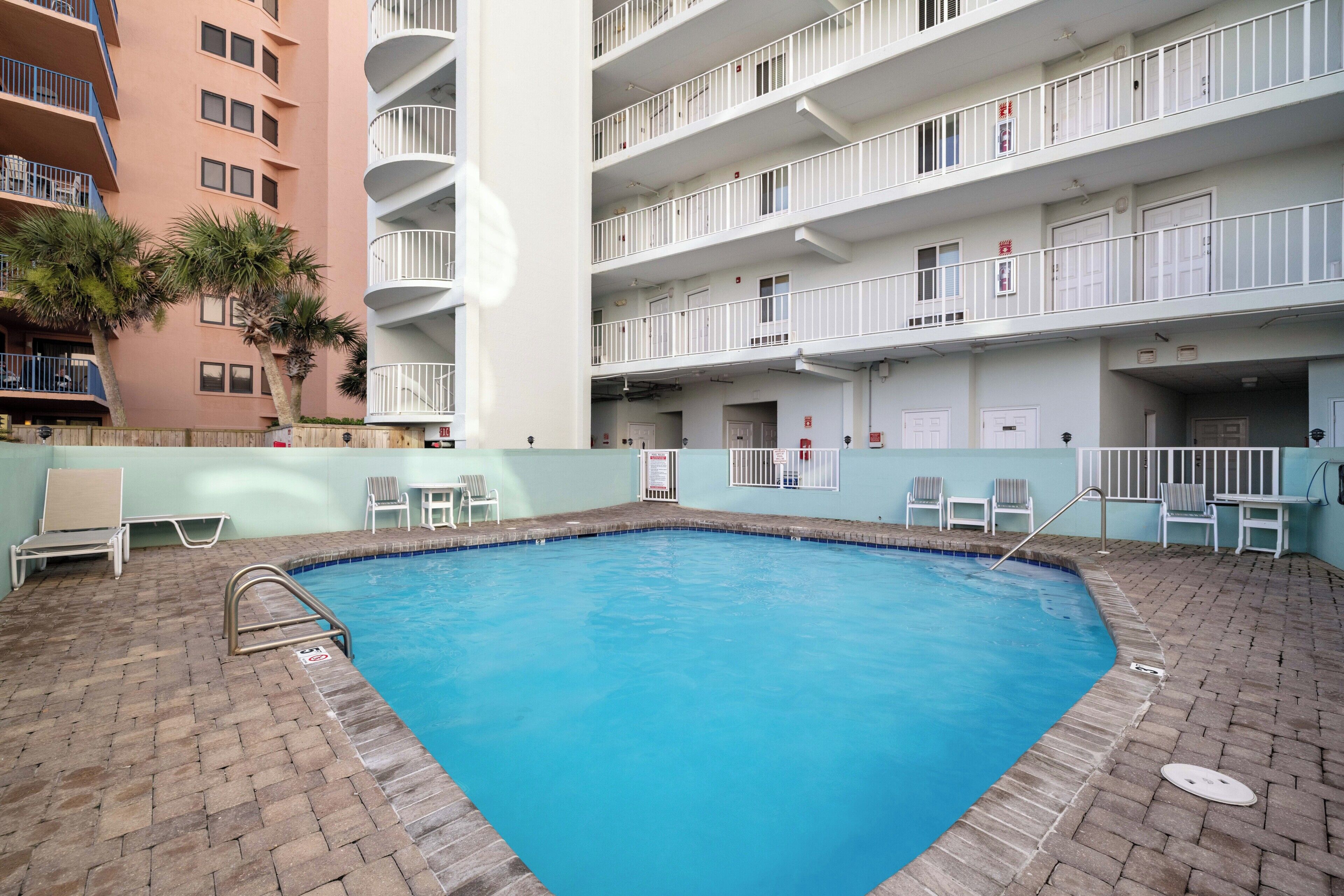 Una piscina interior con piso de ladrillo, rodeada de barandas y sillas blancas.