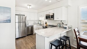 A modern kitchen with white cabinets, stainless steel appliances, a marble countertop, and a small bar area with stools. - Emerald Skye 51 by Liquid Life (Orange Beach)