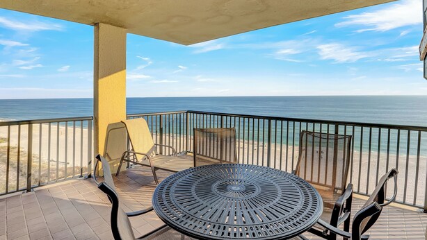 Un balcon avec une table et des chaises rondes en métal, donnant sur une plage et l’océan.