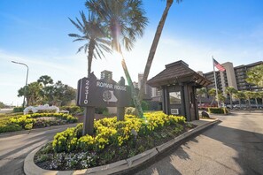 A hotel entrance with a sign, palm trees, and a building in the background.