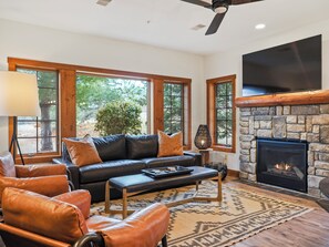Una sala de estar acogedora con chimenea de piedra, mobiliario de cuero y grandes ventanales con vistas al exterior.