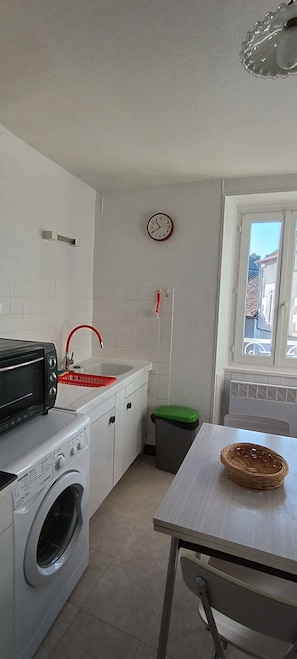 Eine kleine Küche mit Waschmaschine, Toaster, Spüle mit rotem Wasserhahn und einer Uhr an der Wand.