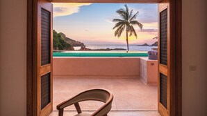 Un balcón con vista a una playa y una palmera al atardecer.