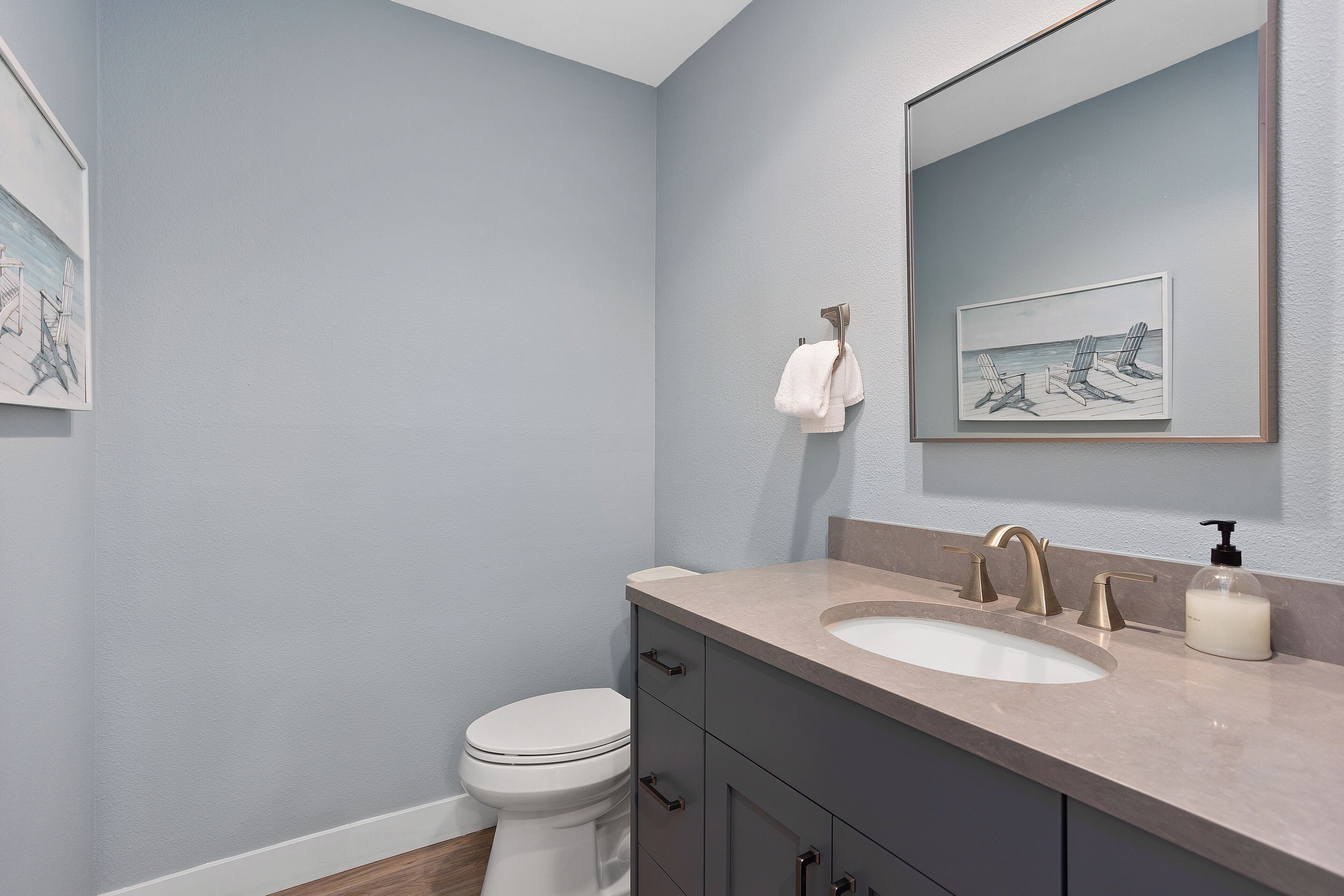 Une salle de bain avec des toilettes blanches, un lavabo beige surmonté d’un grand miroir et une œuvre d’art encadrée accrochée au mur.