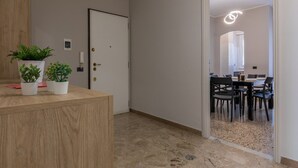 A hallway with a wooden reception desk, potted plants, a door, and a dining area with chairs and a table. - Torino Modern Stay by Wonderful Italy (Torino)