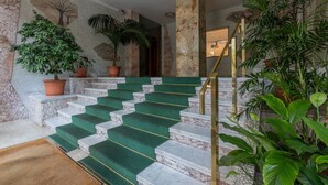 A marble staircase with green carpeted steps, flanked by potted plants and a wall with a tree mural. - Torino Modern Stay by Wonderful Italy (Torino)