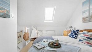 A bedroom with a sloped ceiling, a skylight, a bed with a patterned bedspread, a bedside table with a lamp, and a small sailboat decoration. - Pippin Cottage in Salcombe (Kingsbridge)