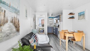 A modern living room with a sofa, a dining table with chairs, and a kitchen in the background. - Pippin Cottage in Salcombe (Kingsbridge)