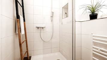 Ein modernes Badezimmer mit weißen Fliesen, einer Dusche, einem Handtuchhalter und einem Topfpflanzen.