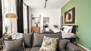 Une chambre d’hôtel moderne avec un canapé gris, un lit avec du linge de lit blanc, un mur d’accent vert et une grande œuvre d’art encadrée.