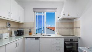 Eine moderne Küche mit weißen Schränken, einem Geschirrspüler, einem Backofen und einem Fenster mit Blick auf eine Stadtlandschaft.