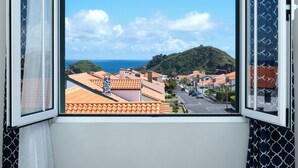 Ein Fenster mit Blick auf eine Küstenstadt, mit terrakottafarbenen Dächern und blauem Himmel.