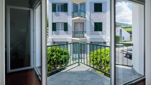 Ein modernes Gebäude mit Glastür, einem Balkon mit grüner Geländer und Blick auf eine Straße mit parkenden Autos.