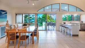 Una cocina moderna con una isla grande, comedor con sillas de madera y vistas al exterior.