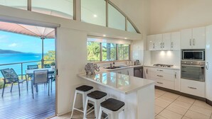 Una cocina moderna con una isla grande, armarios blancos y vistas al mar.