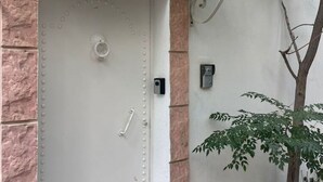 A white door with a handle, a peephole, and a security camera on the wall beside it. - Serenity Home (La Marsa)