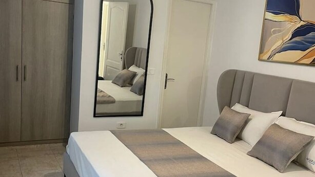 A bedroom with a bed, a wardrobe, a mirror, and a painting on the wall. - Serenity Home (La Marsa)