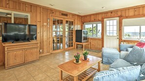 A spacious living room with wooden paneling, a flat-screen TV, a wooden coffee table, and a comfortable blue sofa. - Bayfront in Broadkill Beach (Milton)