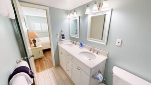 A bathroom with two sinks, a toilet, and a mirror. There is a towel rack with a towel and a small table with a lamp. - Beach House 401d 1 Bedroom Condo (Miramar Beach)