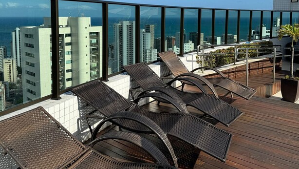 Terraço no telhado com cadeiras de descanso de vime, um deck de madeira e vista para a cidade.