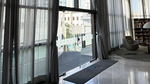 Um hall de hotel moderno com grandes janelas, uma mesa de recepção e uma área de estar.