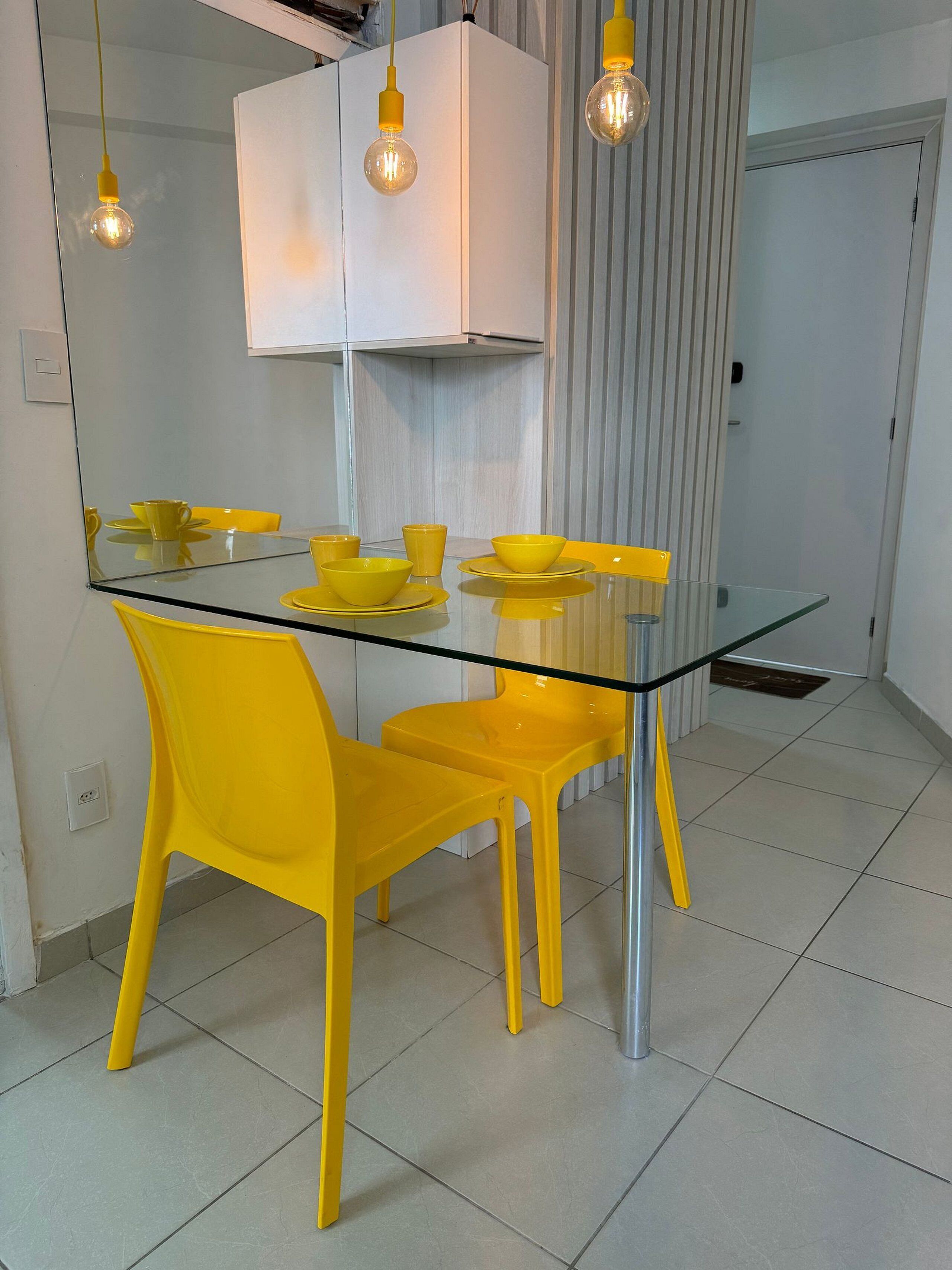 Une cuisine moderne avec une table à manger en verre, des chaises jaunes et des luminaires suspendus.