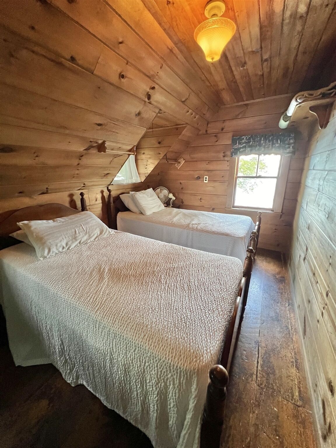 Eine Holzhütte mit zwei Betten, Holzwänden, geneigter Decke und einem Fenster.
