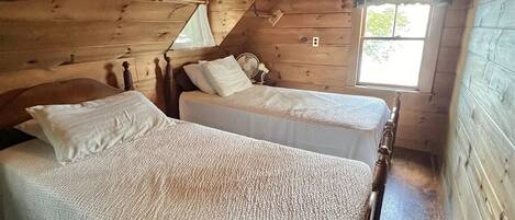 Eine Holzhütte mit zwei Betten, Holzwänden, geneigter Decke und einem Fenster.