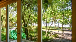 A glass door leading to a balcony with a view of a lush garden and a body of water. - Esterillos Lote 6 Bedroom Home (Parrita)