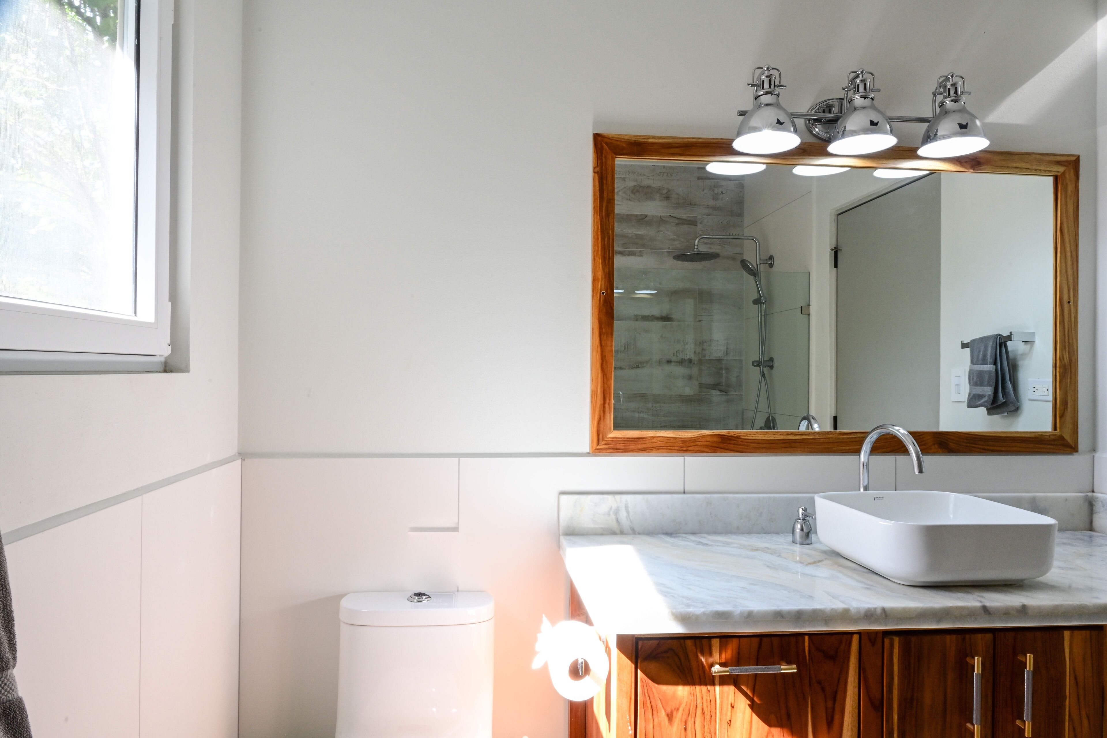 A bathroom with a white sink, wooden vanity, and a large mirror with three lights.