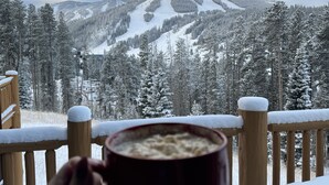A hand holding a mug, overlooking a snowy mountain landscape with a wooden deck and railings. - Antler At Lakota 407 3 Bedroom Home (Winter Park)