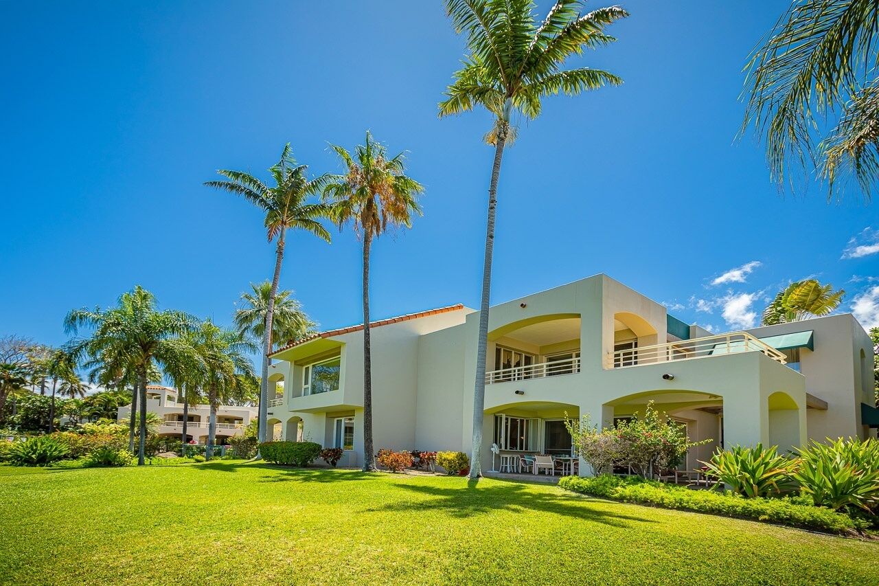 A modern hotel with a two-story structure, featuring balconies and a well-maintained lawn with palm trees.