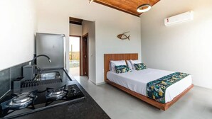 Moderni hotellihuone, jossa on pieni keittiönurkkaus, kuviollinen vuodevaatteilla varustettu sänky ja puinen katto.