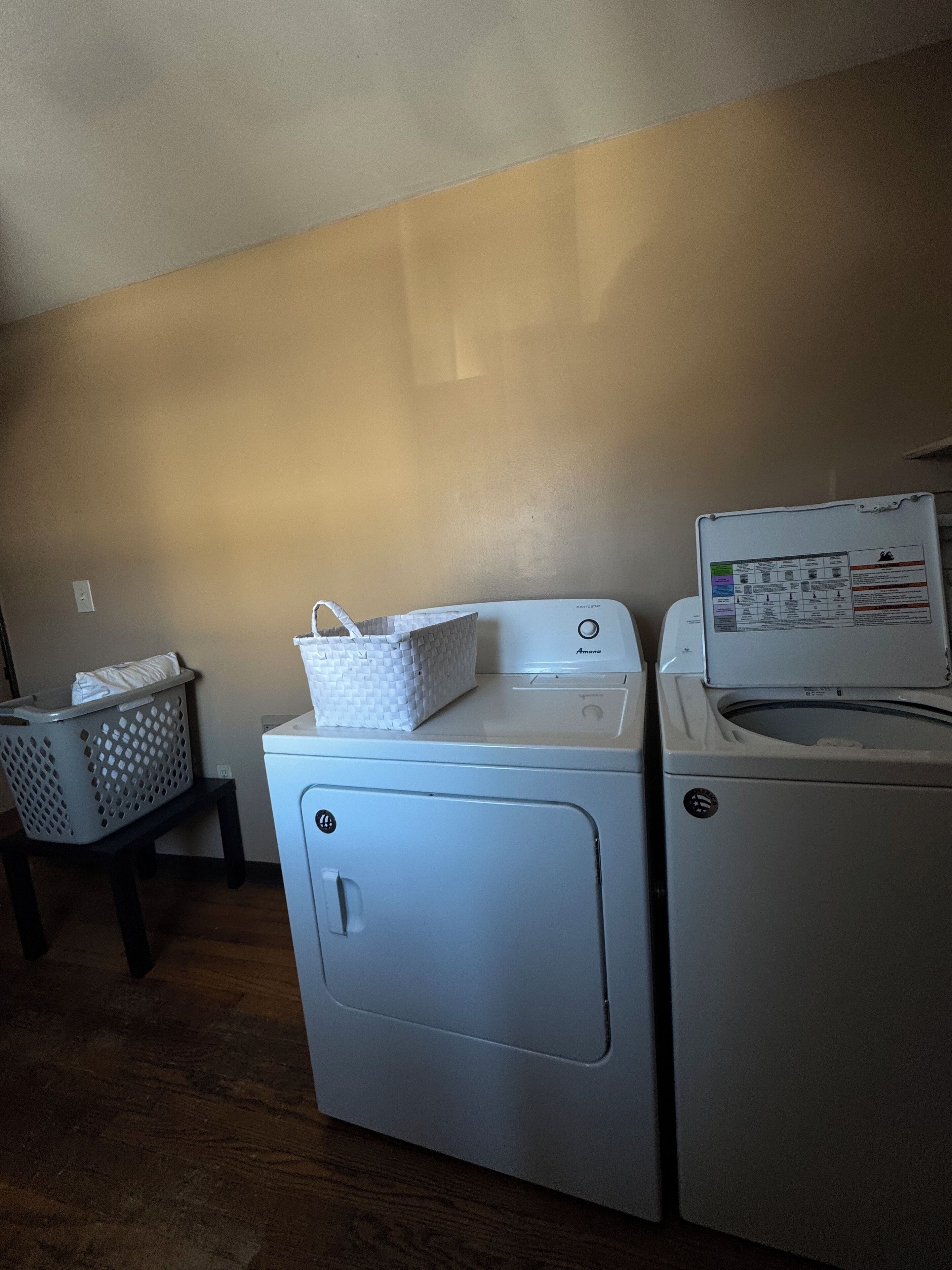 Un espace buanderie comprenant un lave-linge et un sèche-linge, un panier posé sur un tabouret et un panneau de commande fixé au mur.