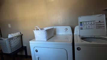 Un espace buanderie comprenant un lave-linge et un sèche-linge, un panier posé sur un tabouret et un panneau de commande fixé au mur.