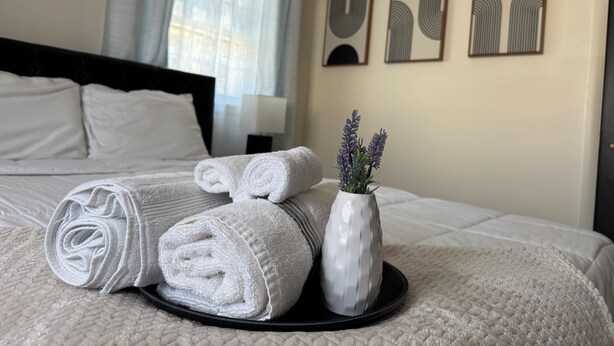 A neatly made bed with rolled white towels and a vase with lavender flowers on a tray. - 1bd apt, 2 min walk to Albany med, off street parking and washer/dryer (Albany)