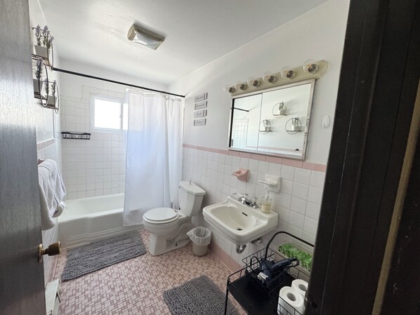 A bathroom with a toilet, sink, and shower. There are towels and a trash can.
